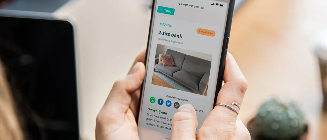 Vrouw bezoekt op haar telefoon de website van Goods for Refugees en kijkt naar een advertentie waar een bank aangeboden wordt