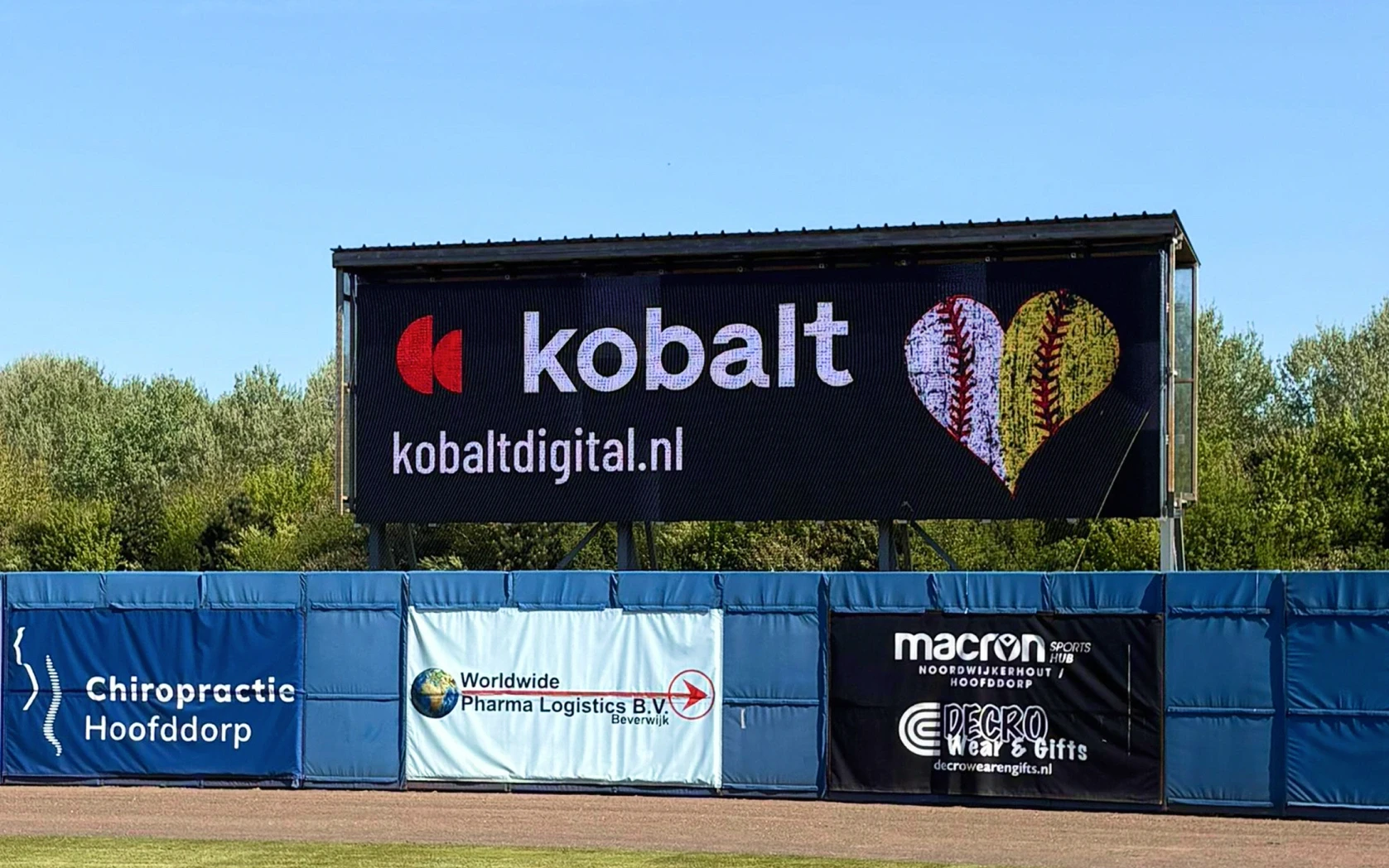 Kobalt Digital LED-scherm langs het softbalveld met logo en de tekst kobaltdigital.nl tijdens Softball Against Cancer