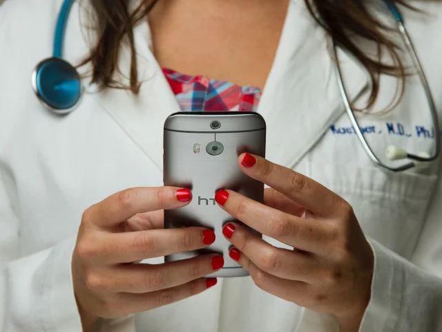 Een ziekenhuismedewerker met een stethoscoop om haar nek en een mobiele telefoon voor haar vast