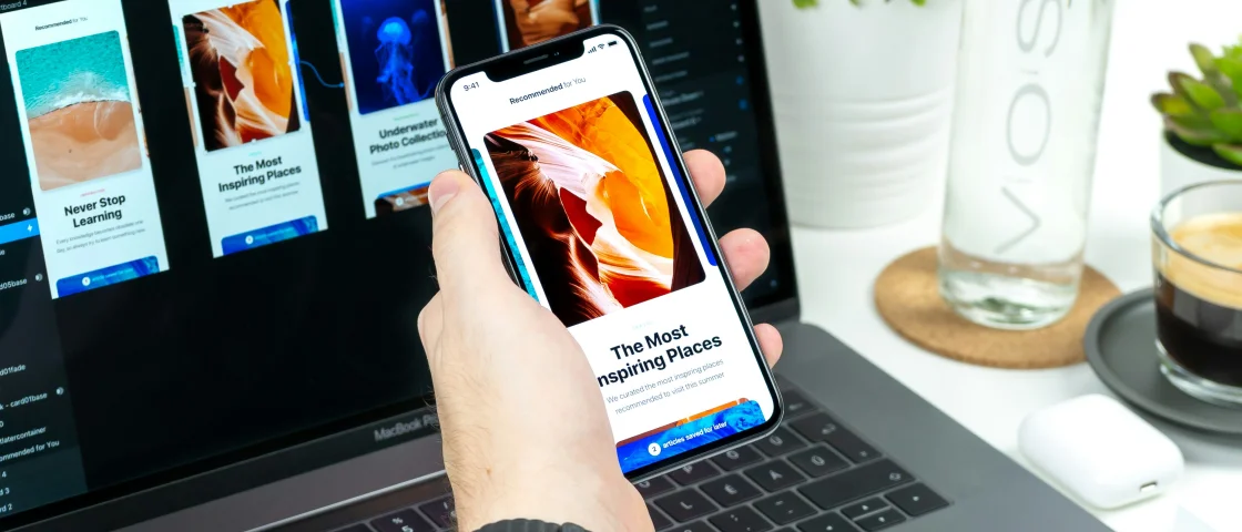 Macbook met een ontwerp open en een hand met een mobiel met daar hetzelfde design open