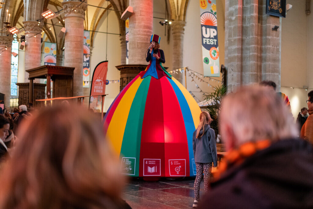 Vrouw op stelten met een enorme rok in de kleuren van een circustent is aan het zingen